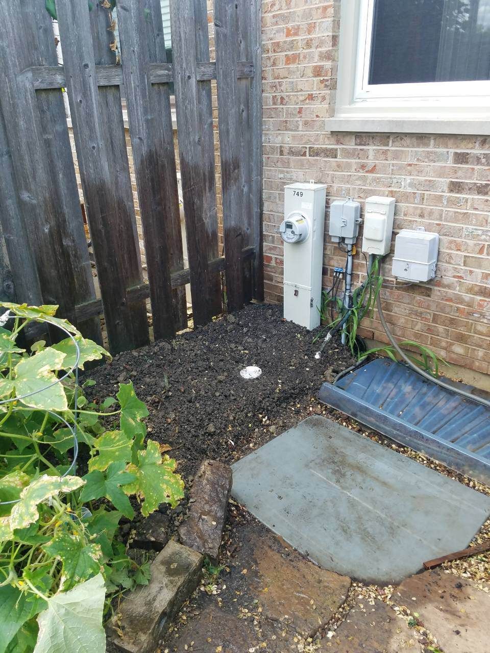 Corner of yard with fence, brick building, electrical boxes, stone path, and mulch bed.