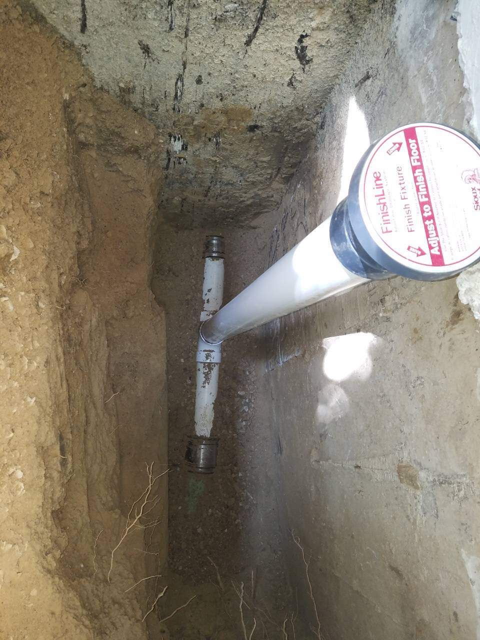 White PVC pipes in a narrow trench, with a T-fitting, and a label at the end.