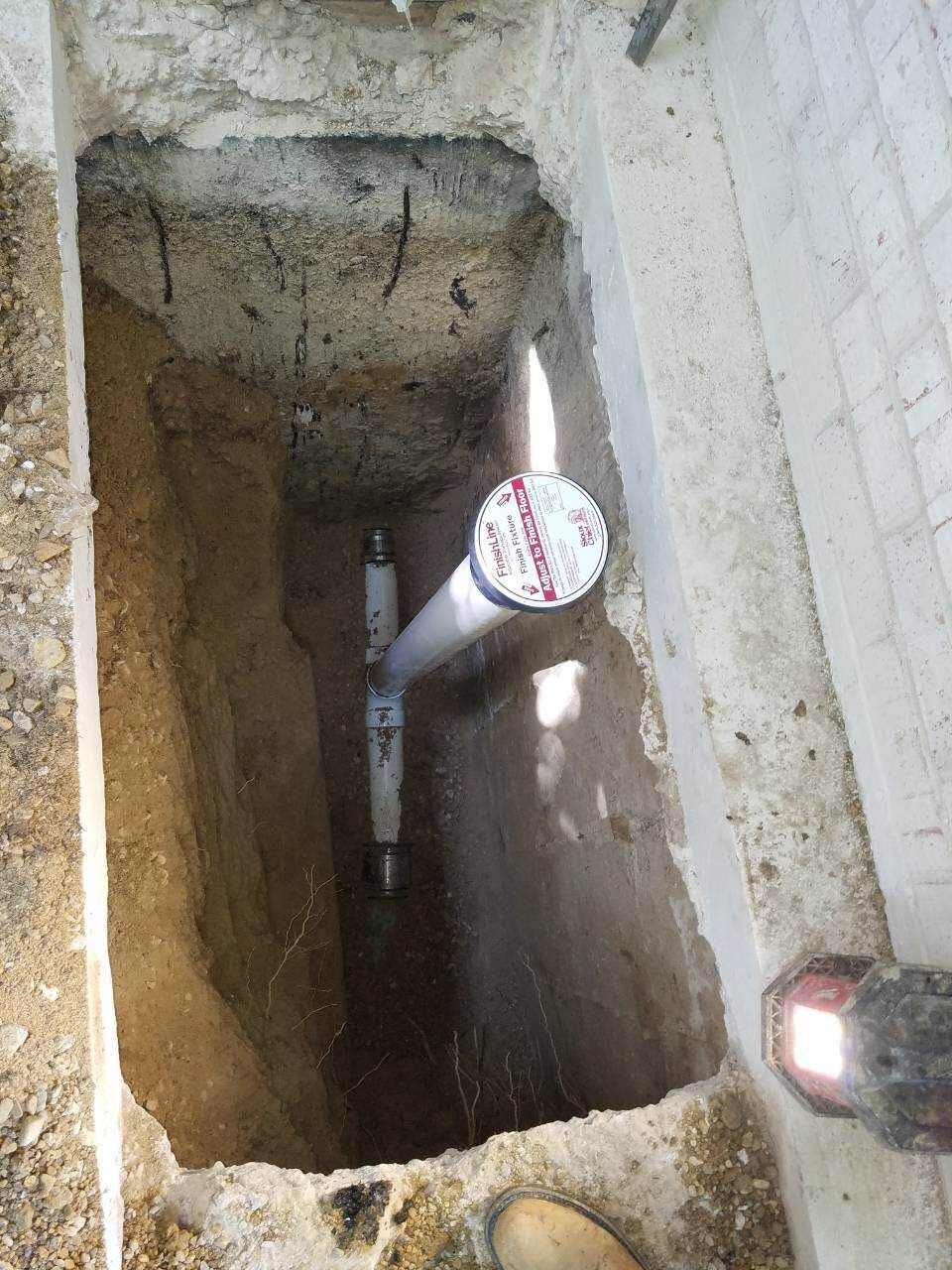 Trench with PVC pipes and a valve; ground and concrete surrounding.