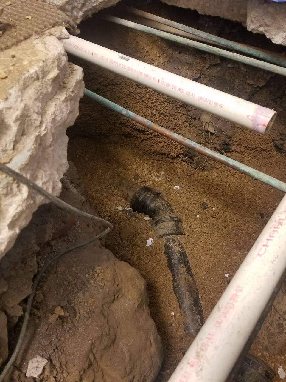 Pipes in a sandy trench under a broken concrete structure. PVC and copper pipes are visible.