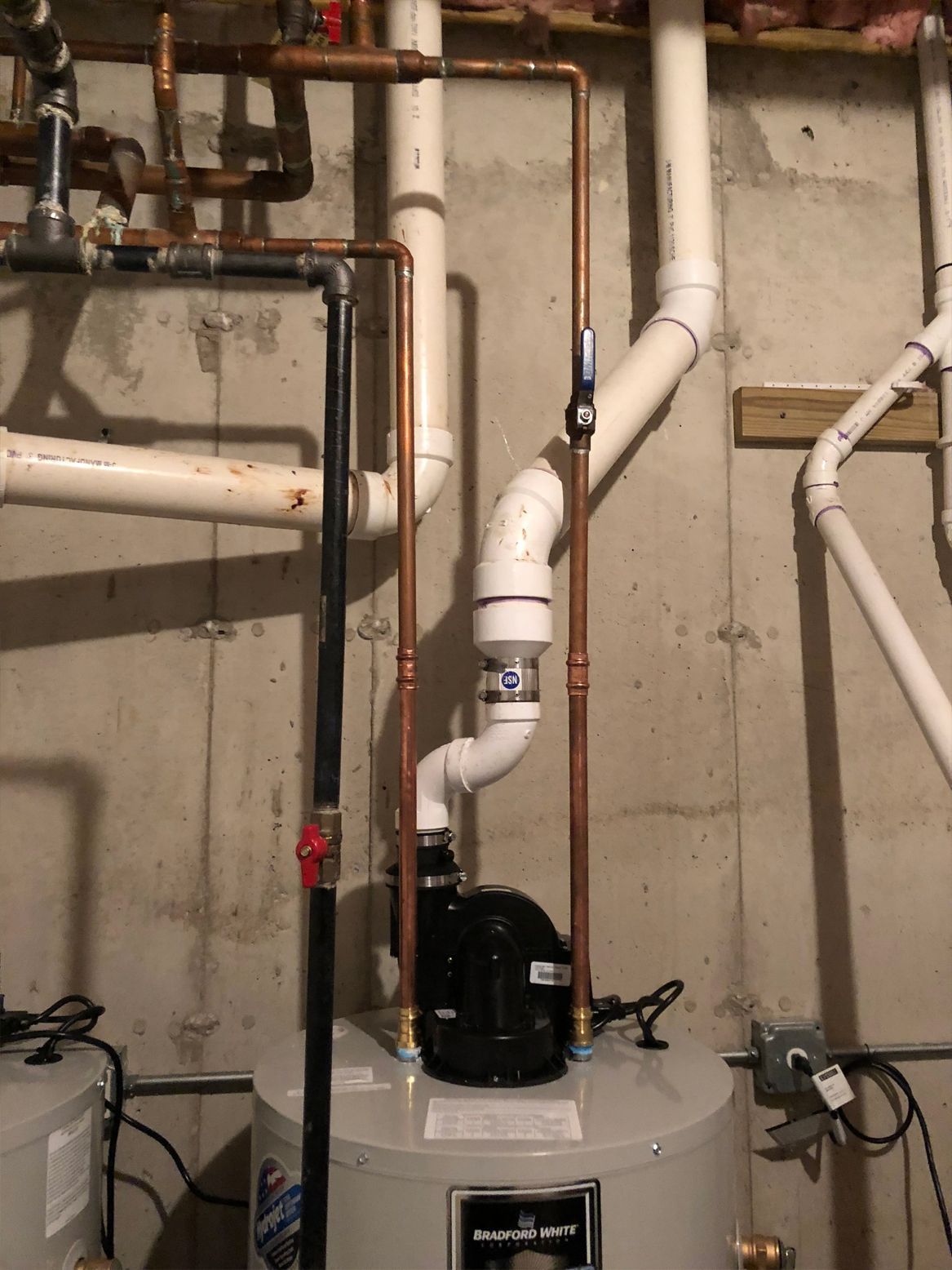 Water heater with copper and PVC pipes against a concrete wall.