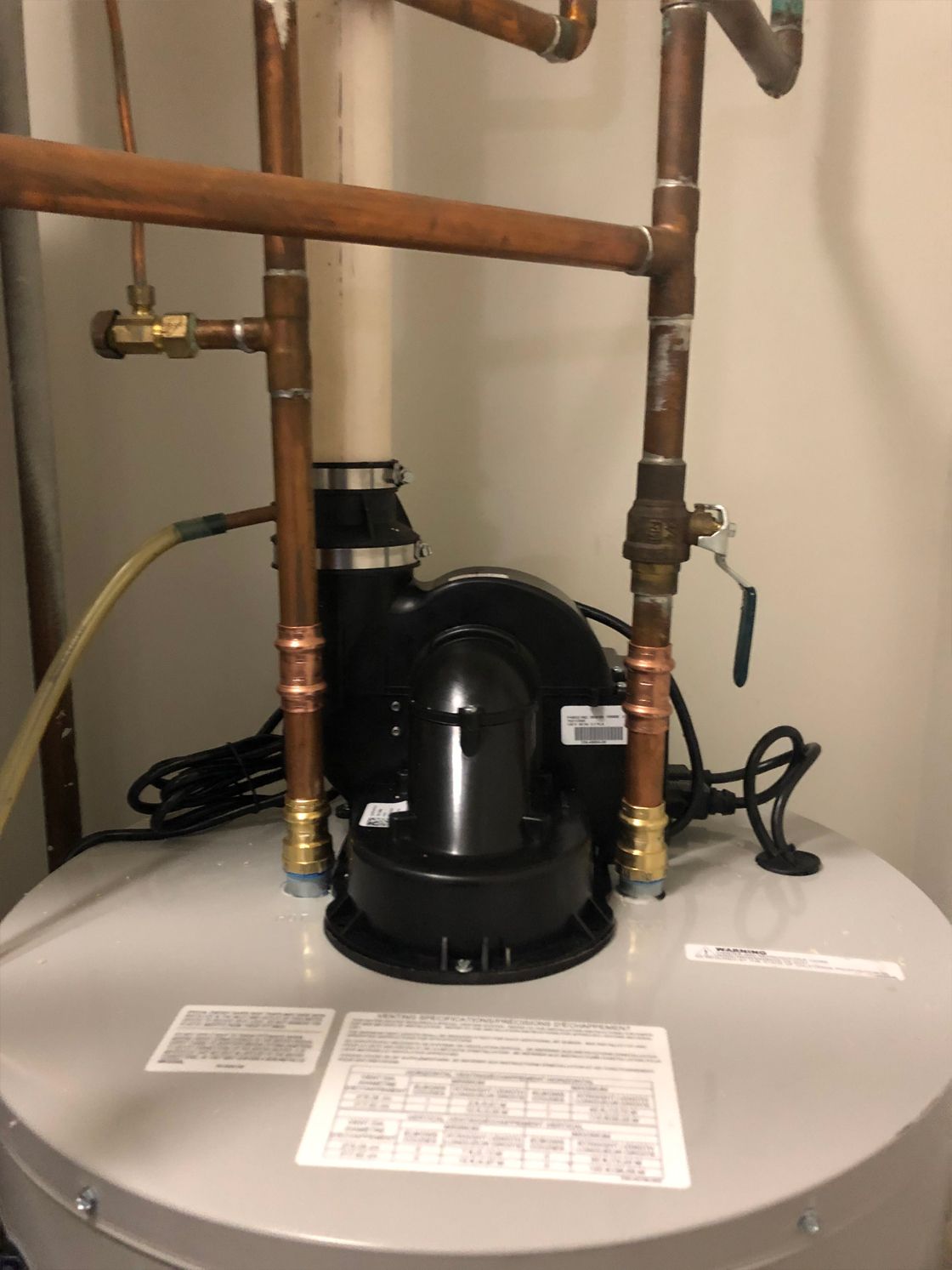 A water heater with copper pipes, a black exhaust fan, and connecting wires.
