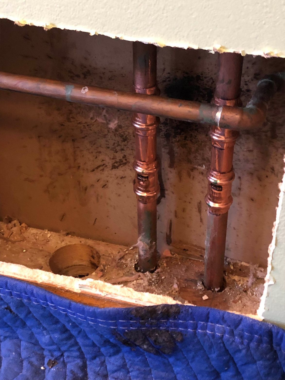 Copper pipes inside a wall cavity with soldered joints and dark staining.