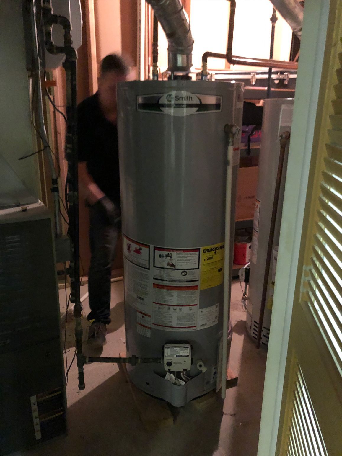 Person standing near a tall, cylindrical water heater in a basement.