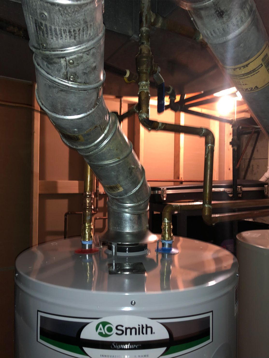 A.O. Smith water heater with copper pipes and metal flue in a basement.