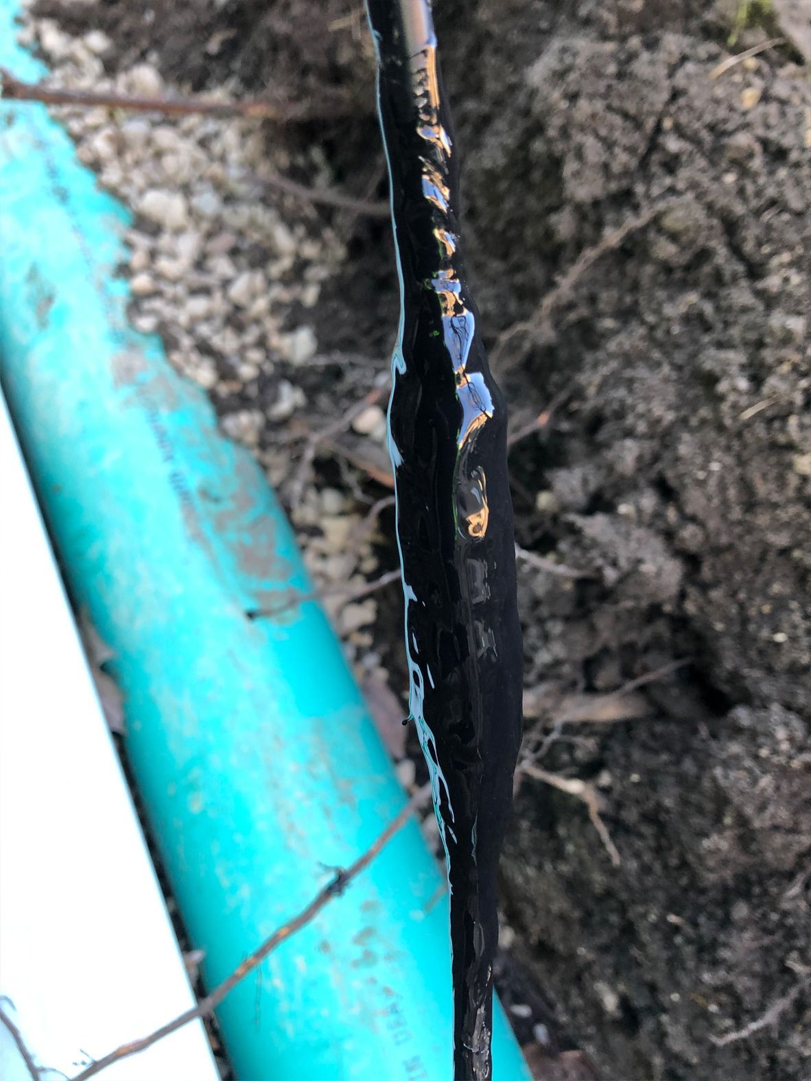 Black cable with dripping sealant near a turquoise pipe in a dirt setting.