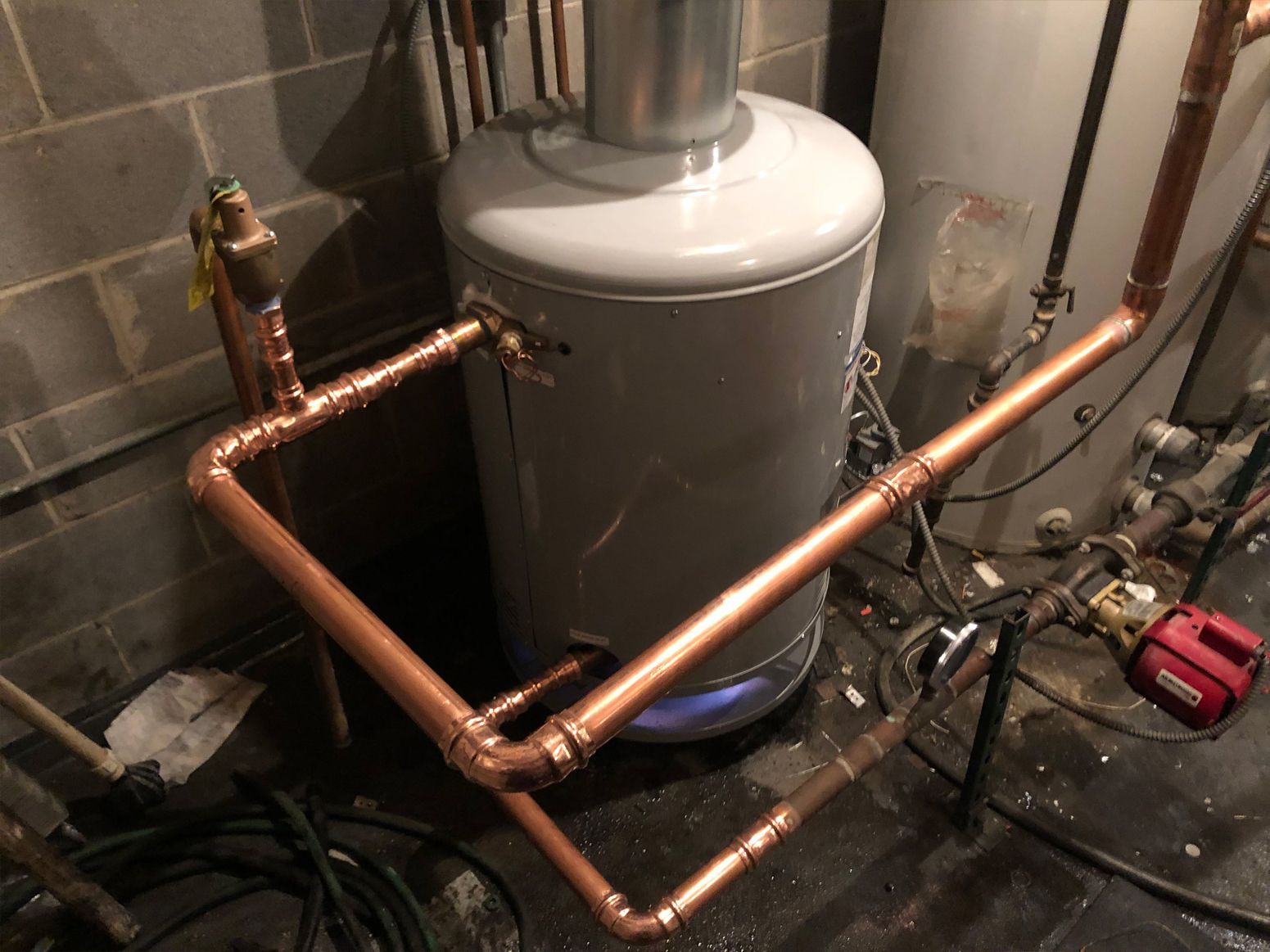 Copper pipes connected to a hot water tank in a basement setting.