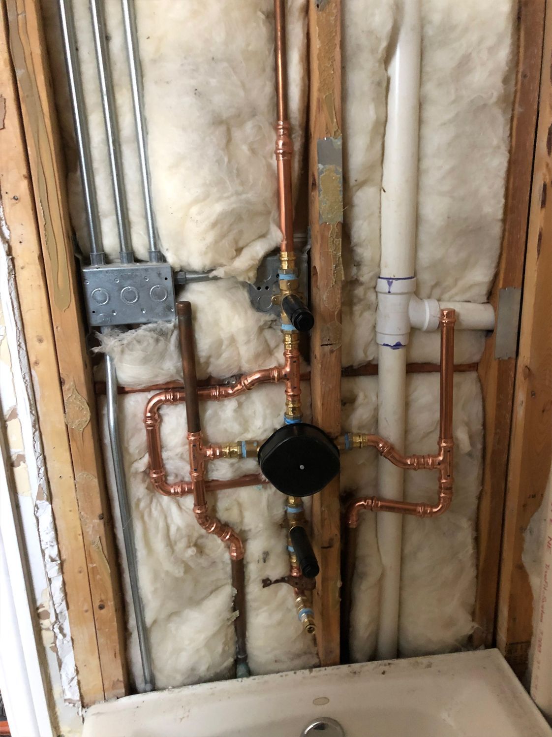 Copper pipes and plumbing fixtures installed inside a wall, near a bathtub.