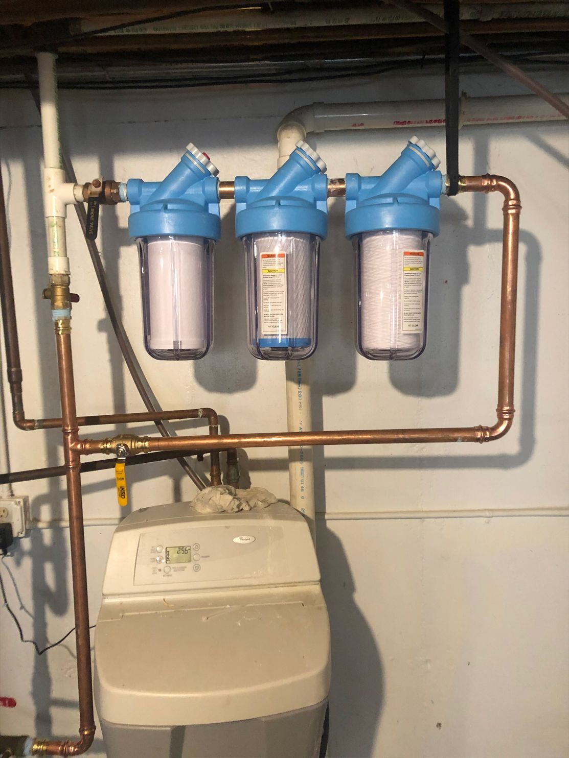 Water filtration system with three blue filter housings, copper pipes, and a water softener.