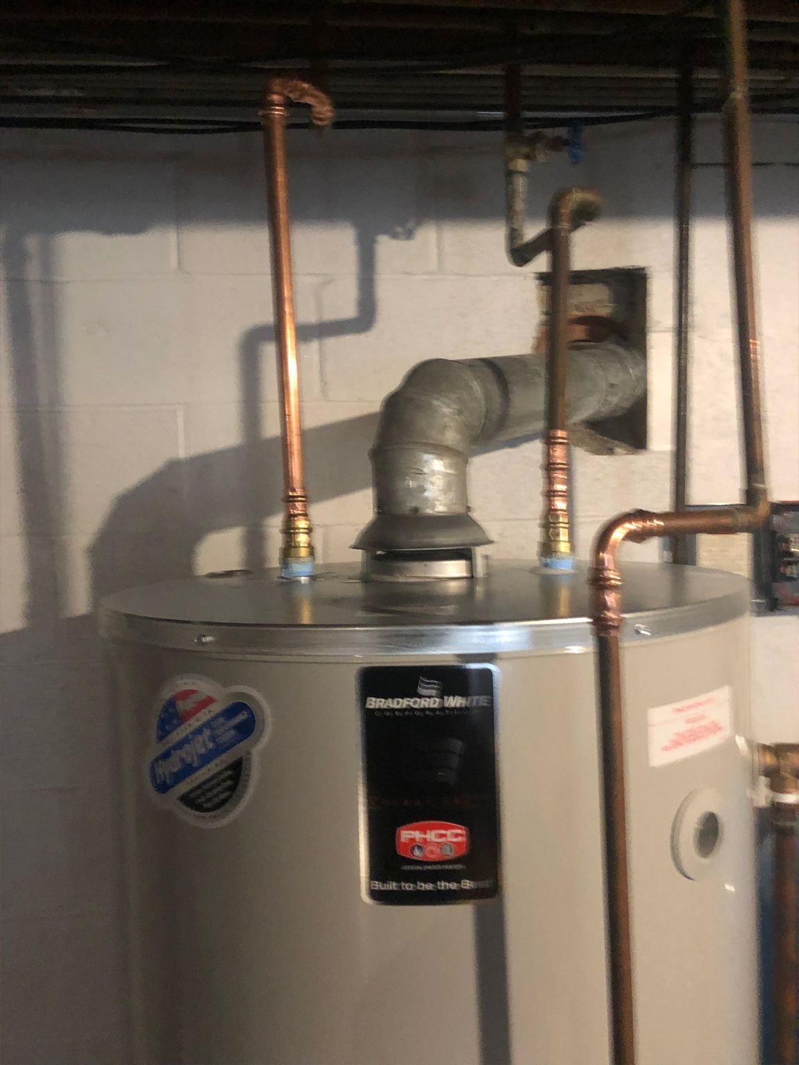 A water heater with copper pipes in a basement setting.