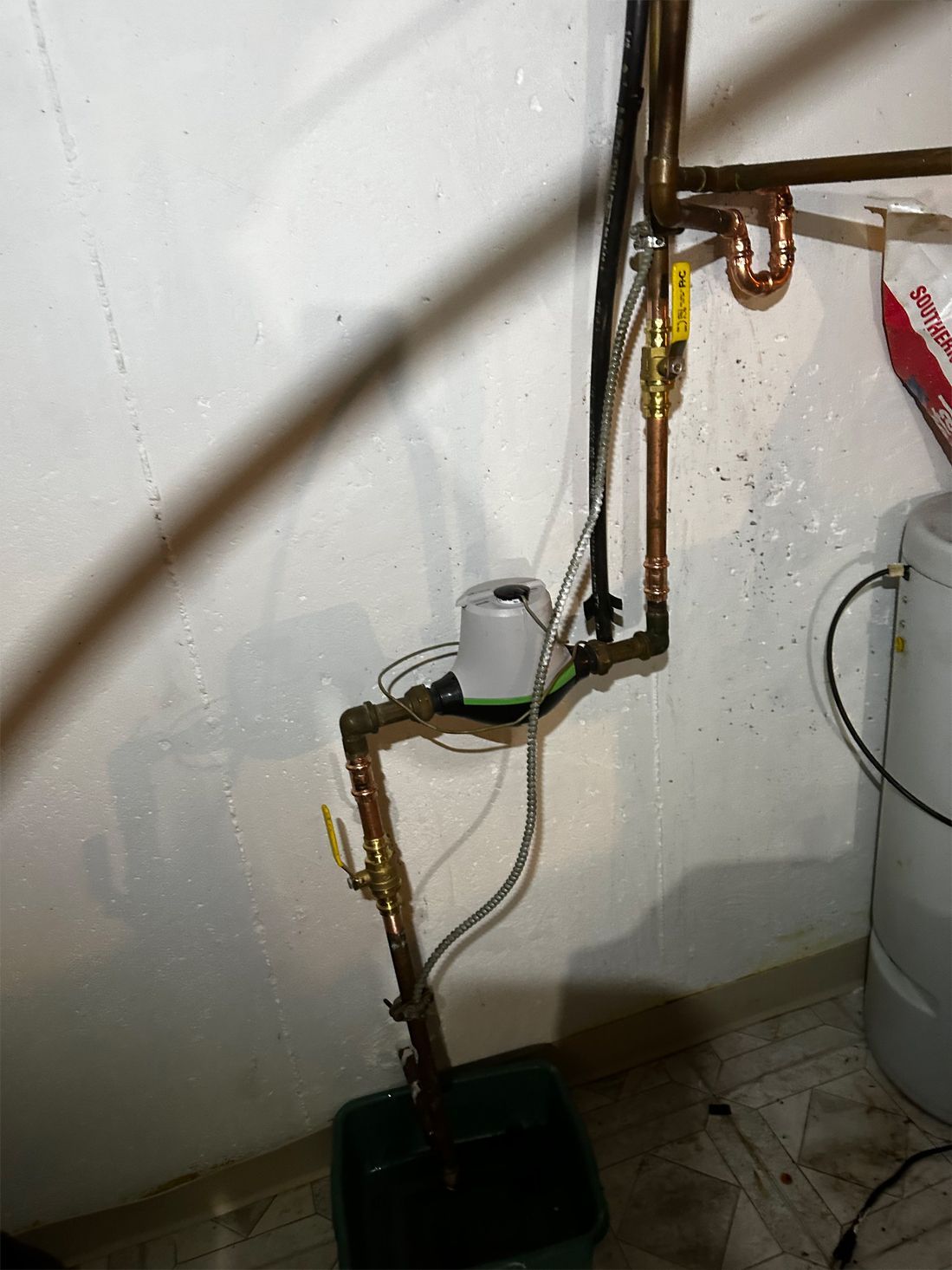 Copper pipes with a water meter and drainage bucket in a basement.