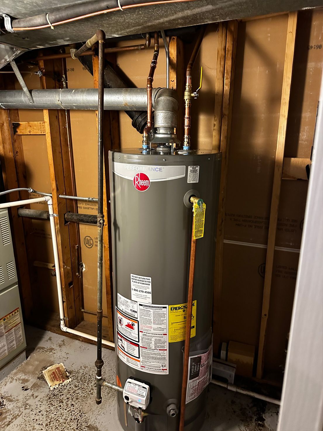 Water heater in a utility room; copper pipes and wooden framing visible.