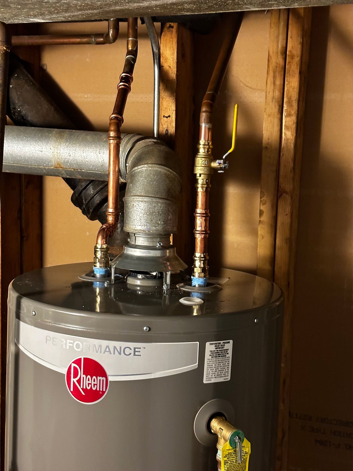 A Rheem water heater with copper pipes in a room with wood framing.