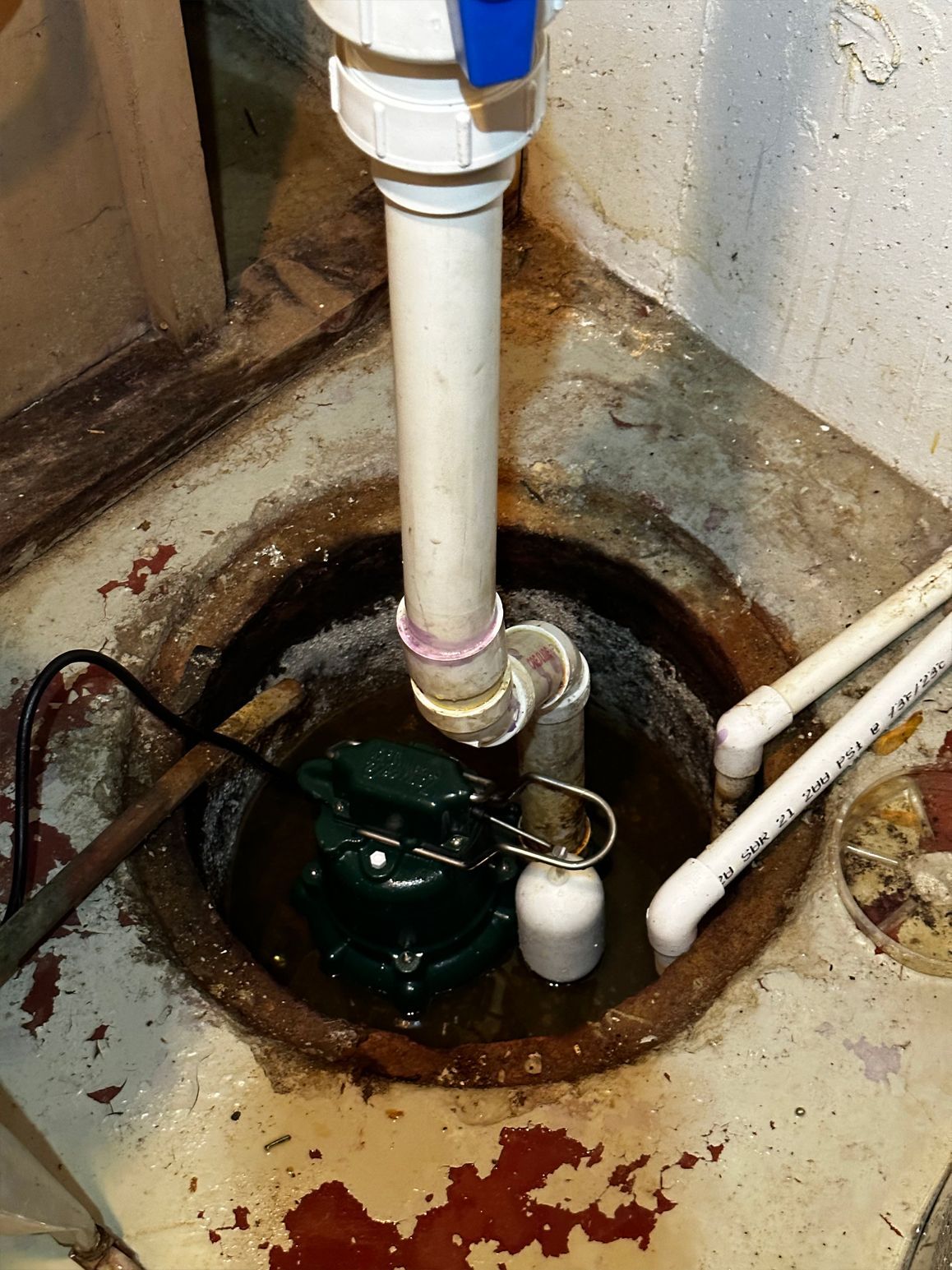 Sump pump in a concrete pit with water, white PVC pipes, and a blue valve.