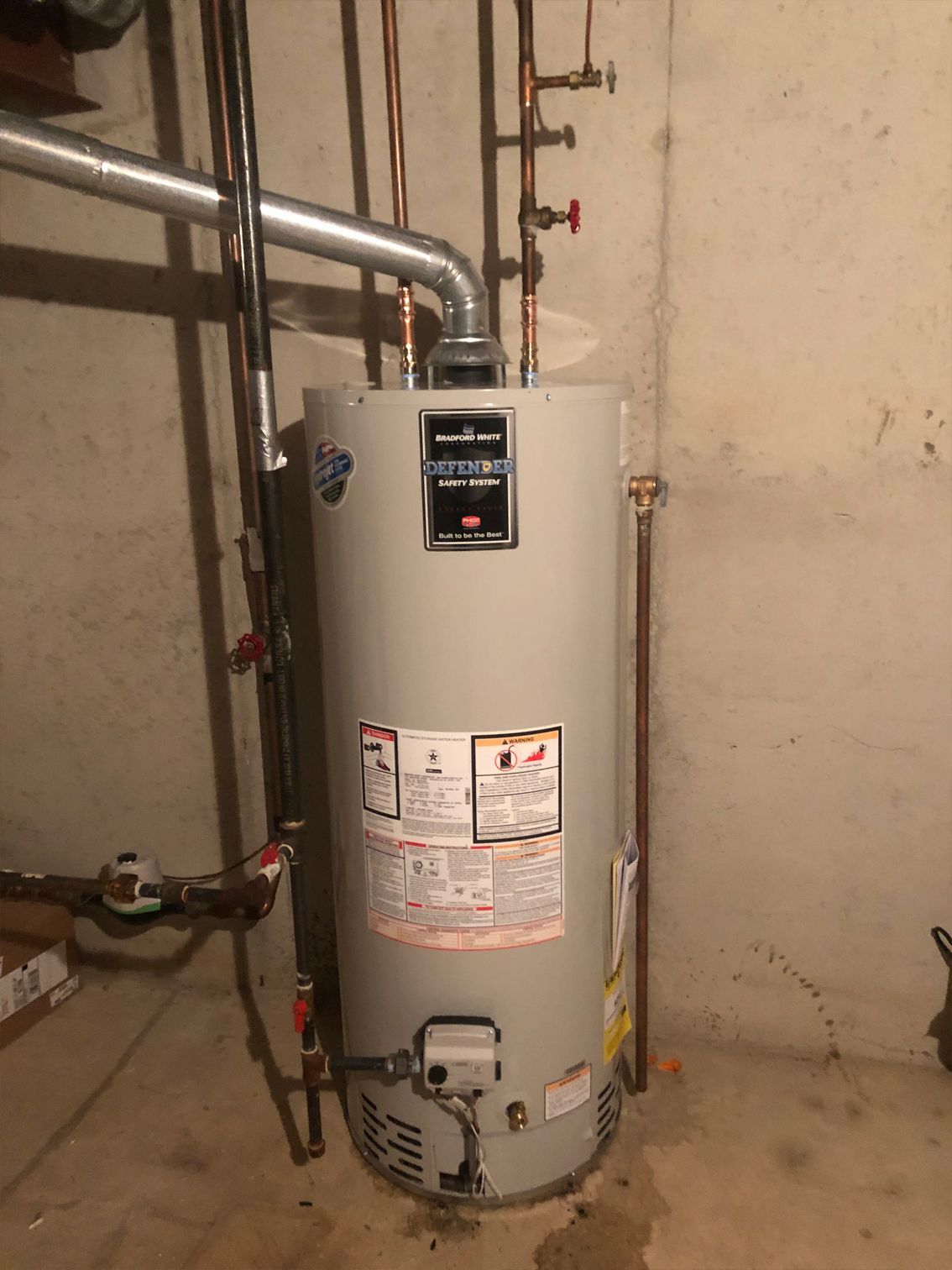 Tall, cylindrical water heater in a basement with metal vent and copper pipes.