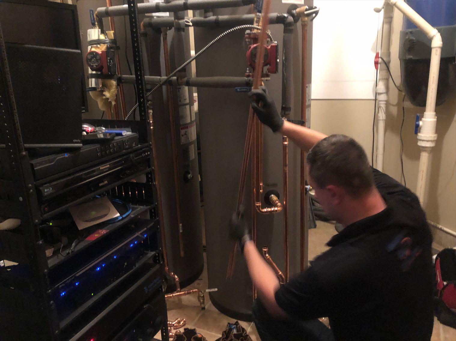 Plumber working on copper pipes near water tanks in a room.