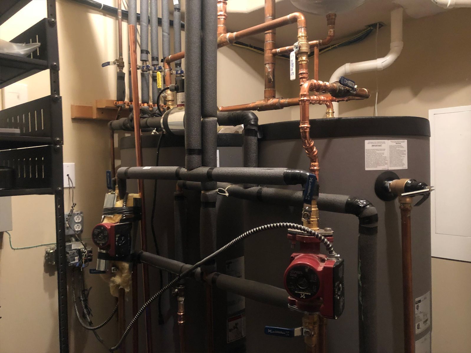Plumbing system with copper pipes, black insulation, and red pumps in a utility room.