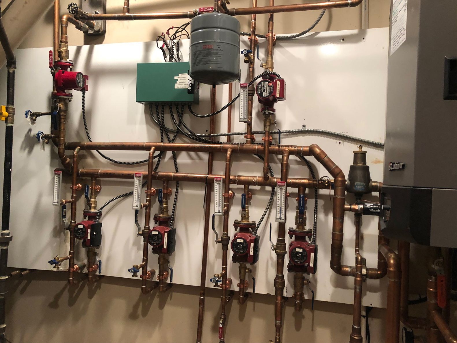 Copper pipes and red pumps of a hydronic heating system on a white wall.