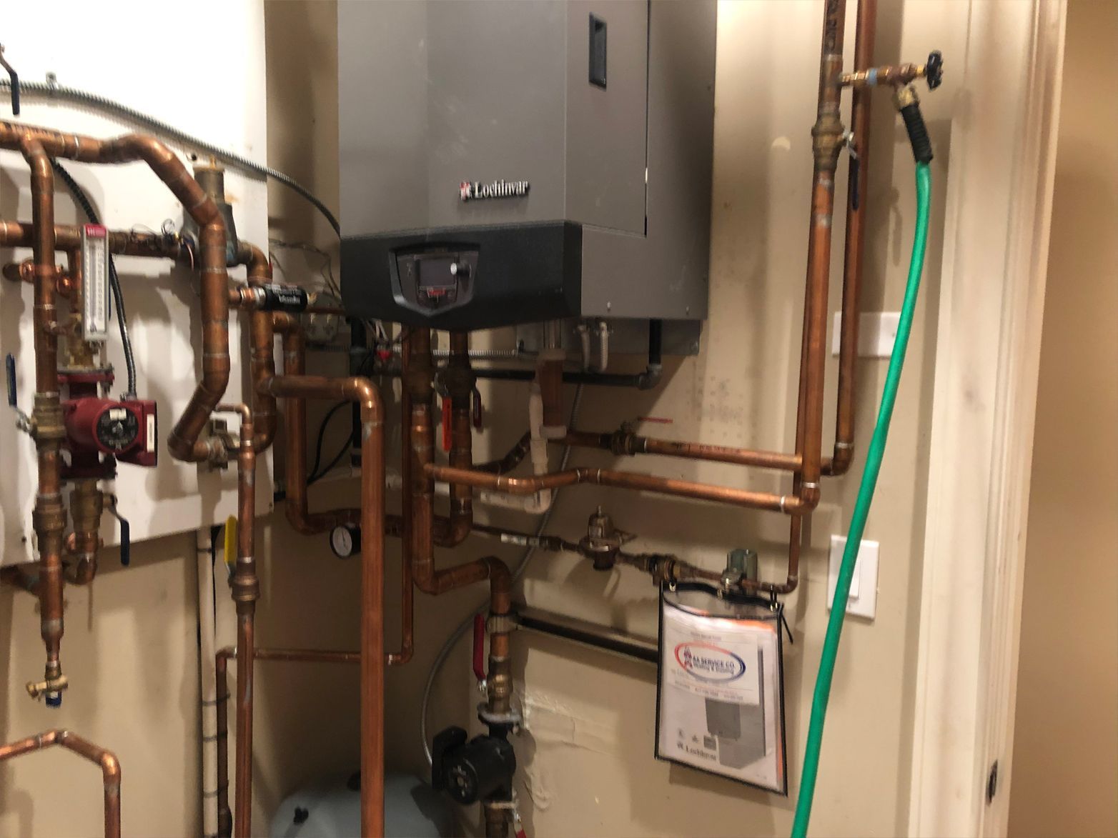 Gray wall-mounted boiler with copper pipes and green hose attached.