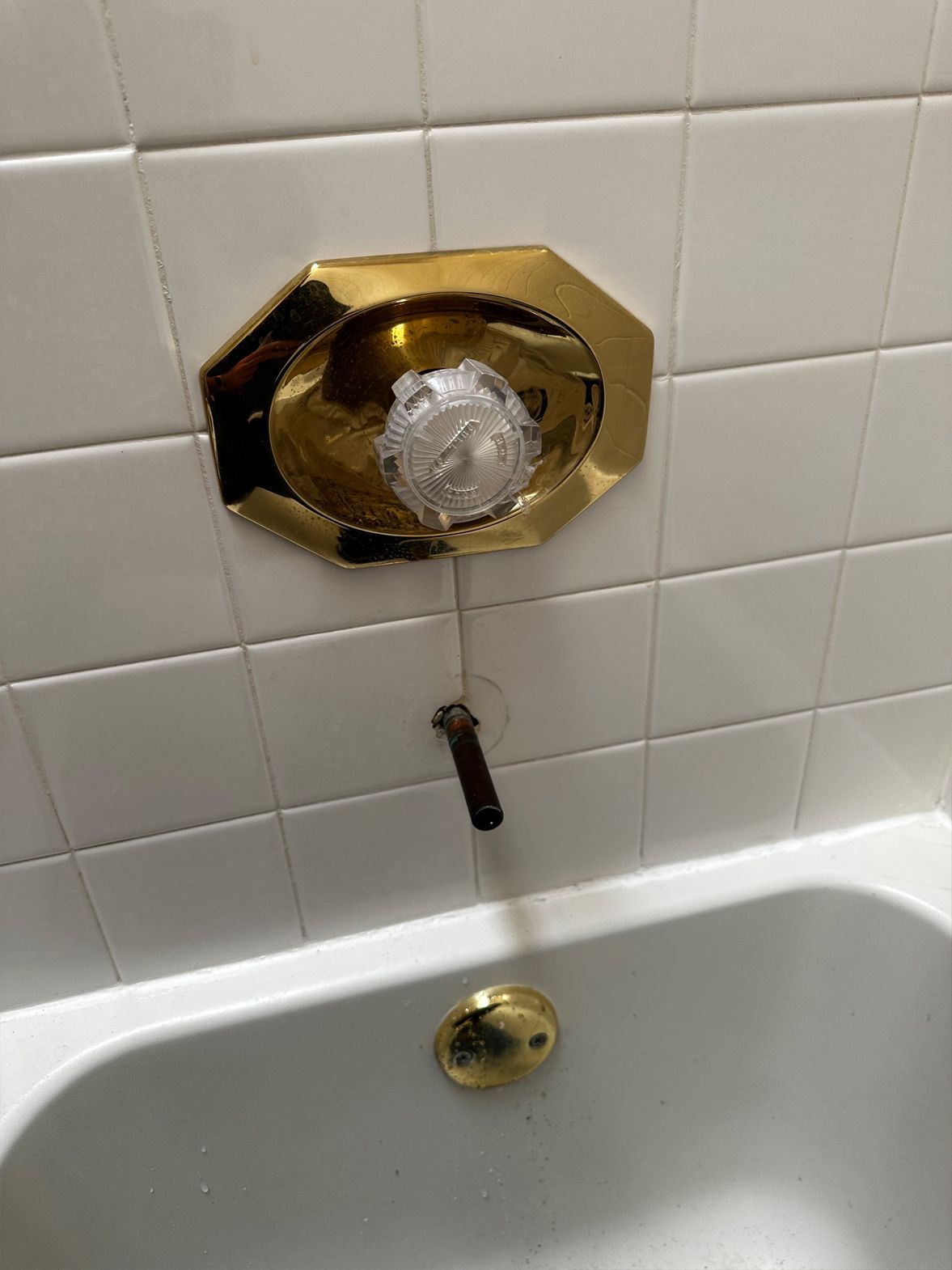 Bathtub faucet with gold-colored fixtures against a white tiled wall. Spout and drain visible.