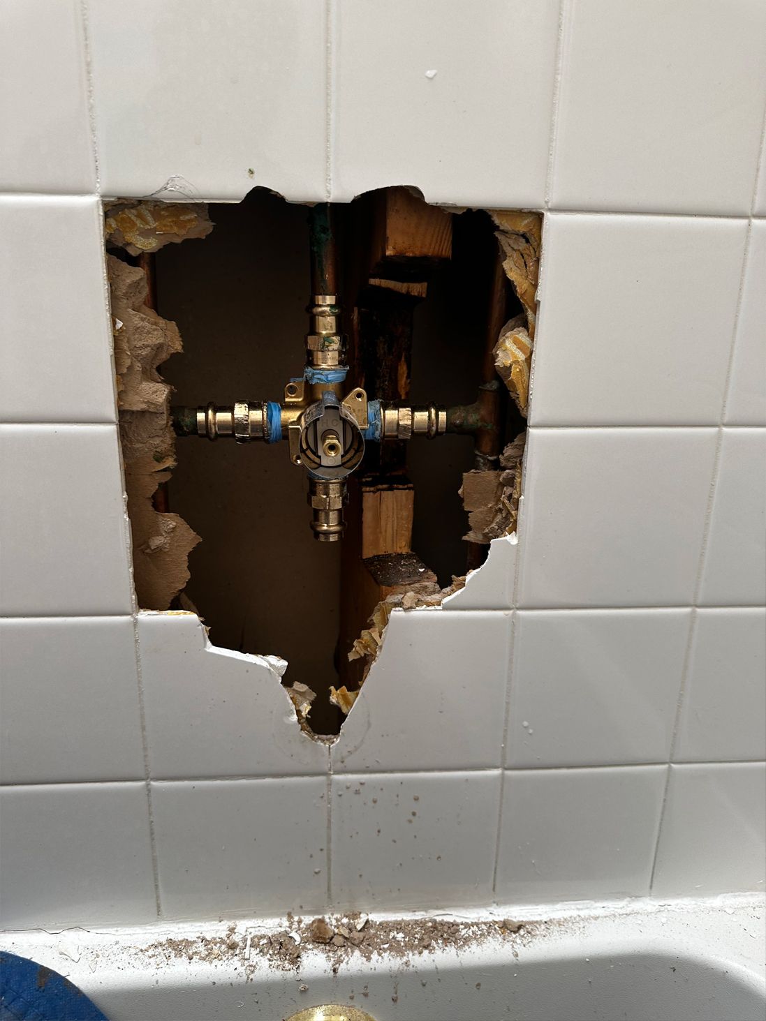 Hole in tiled wall exposing plumbing fixtures, likely a shower valve.