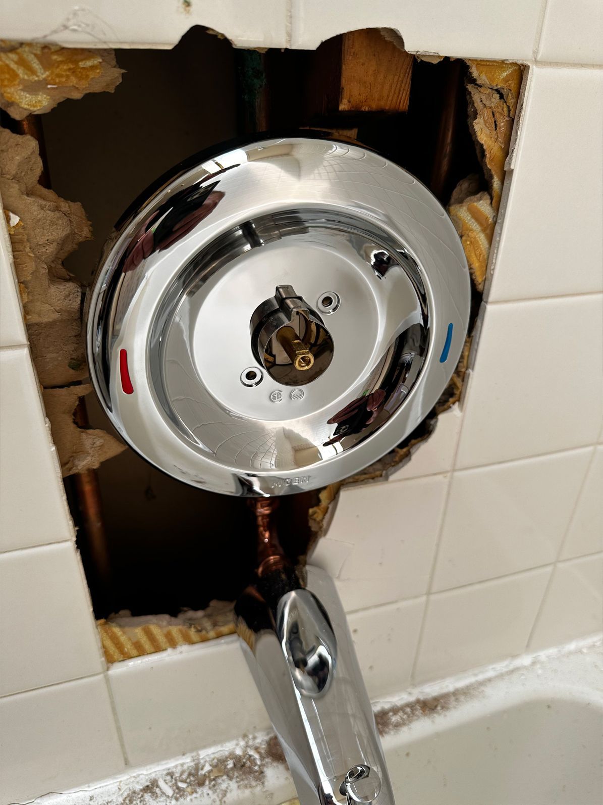 Chrome shower faucet with exposed plumbing in a tiled wall.