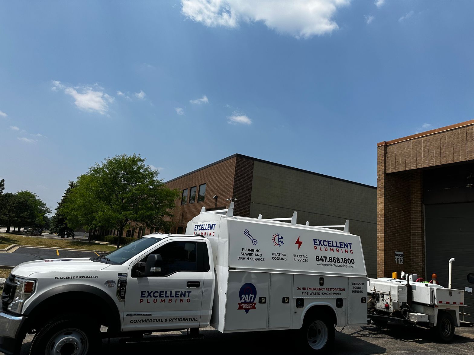 White work truck with company logos parked in front of a brick building on a sunny day.