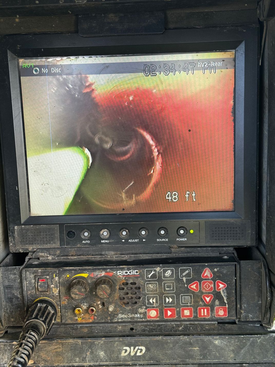 Screen displaying a pipe inspection camera view, showing a red and brown pipe interior. Control panel below.