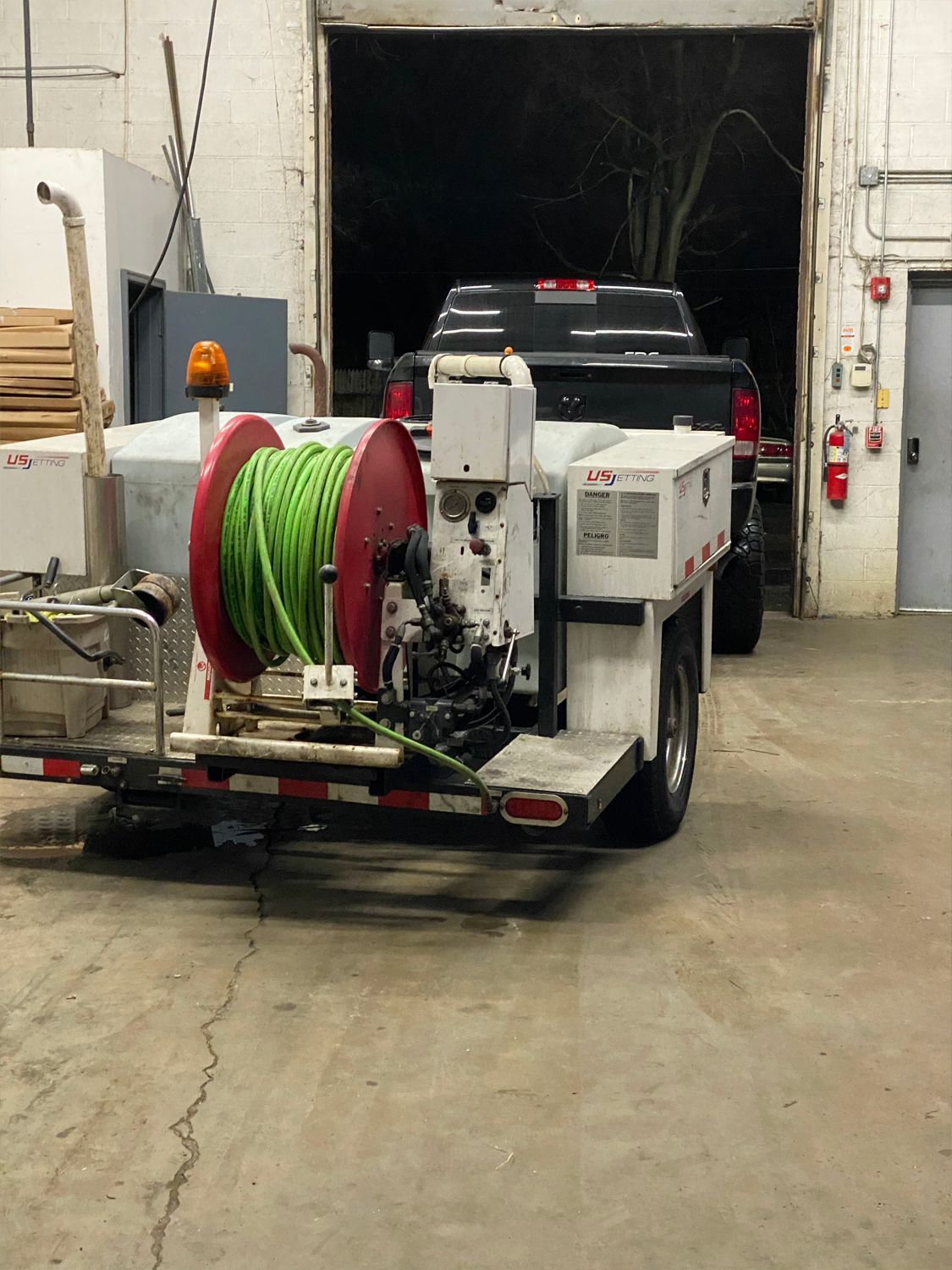 A trailer with green hose reel and water tank inside a garage. A truck is parked behind it.