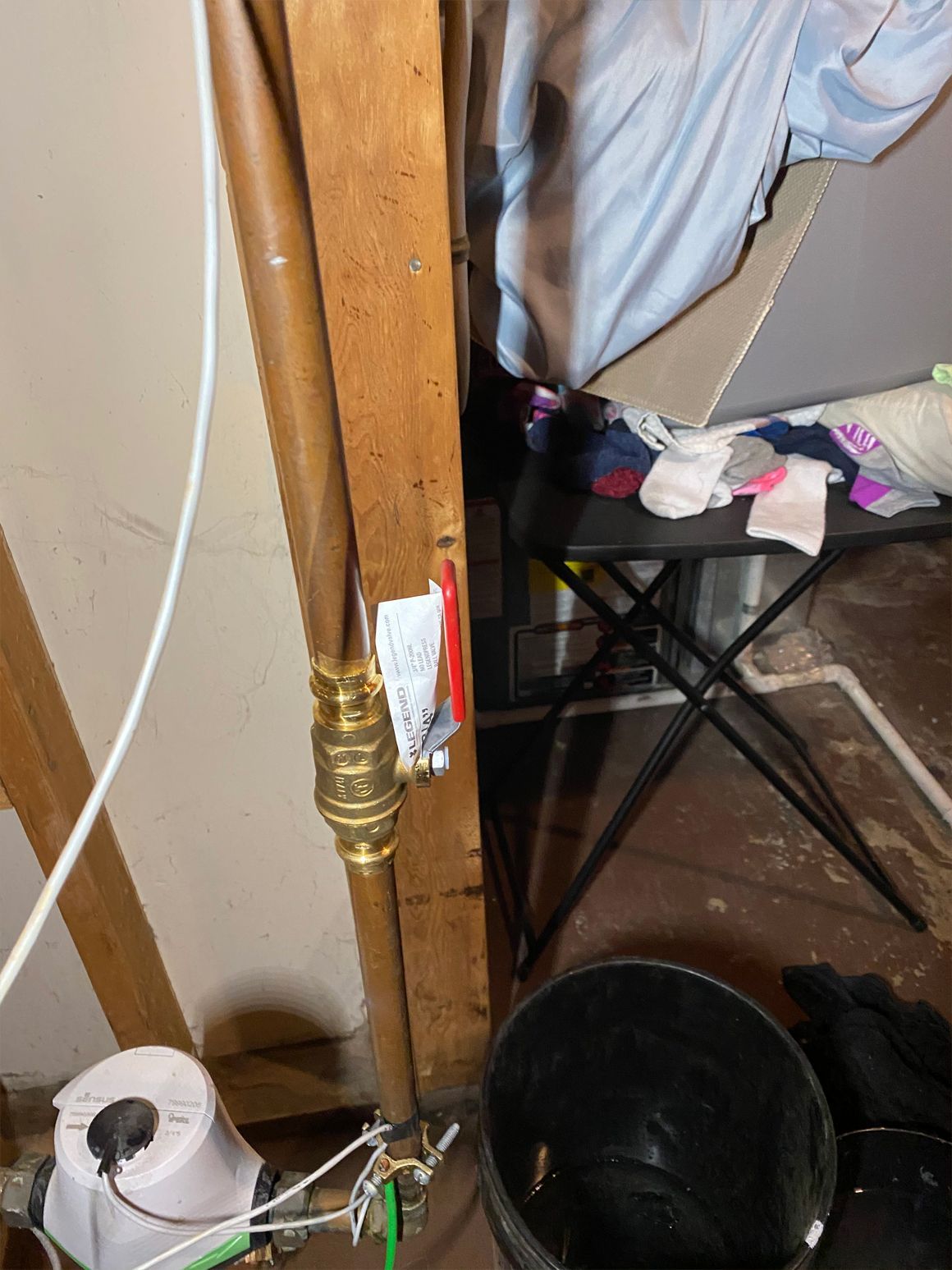 Copper pipes with a brass pressure regulator are mounted to a wooden stud in a basement setting.