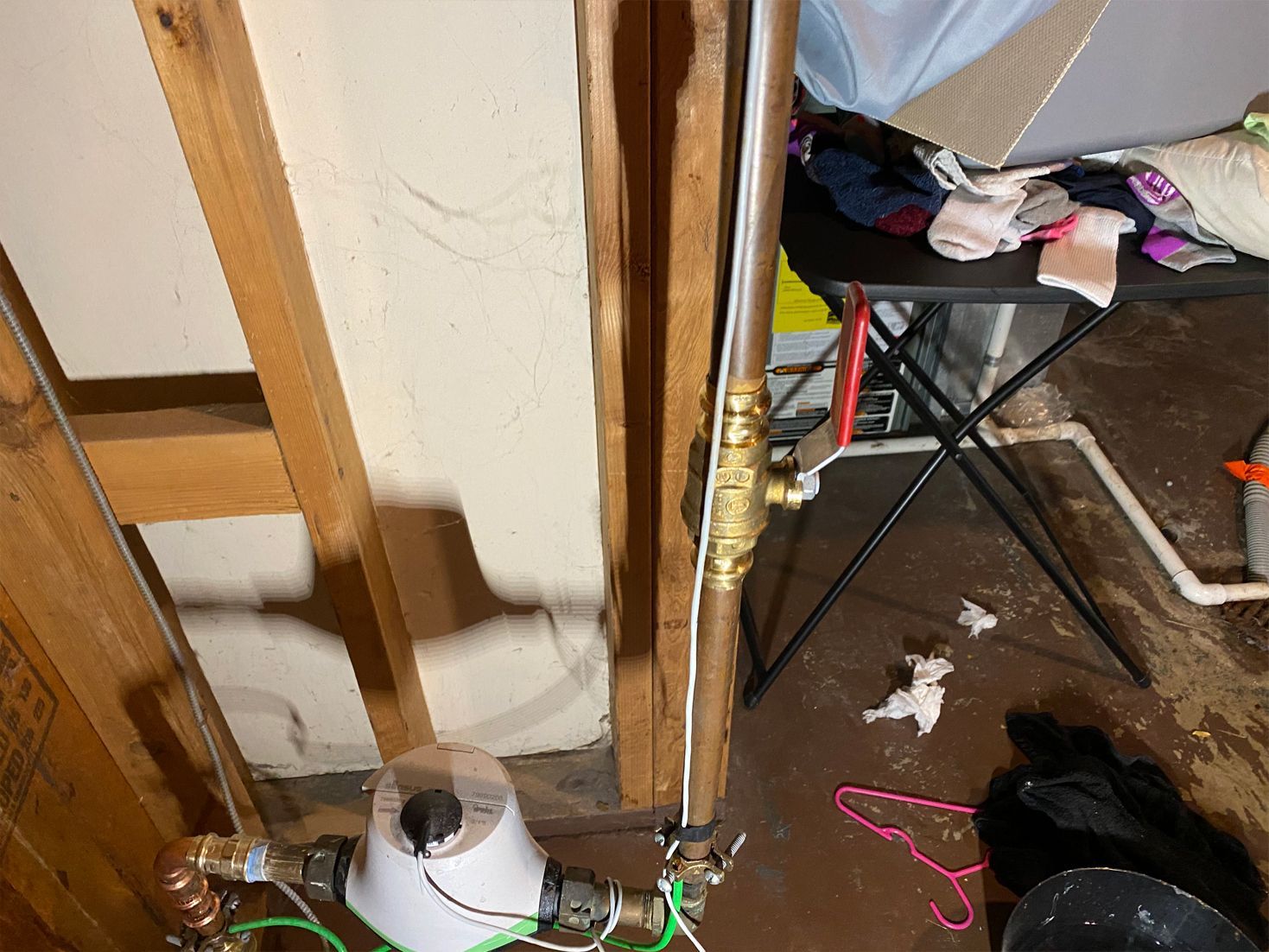 Water meter and pipes within a wall's frame, against a messy basement background.