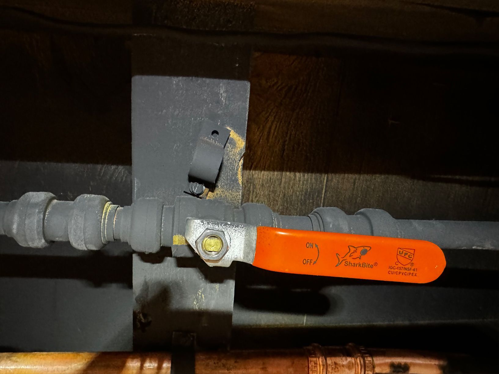 A grey gas pipe with an orange valve and a broken pipe strap against a dark wall.
