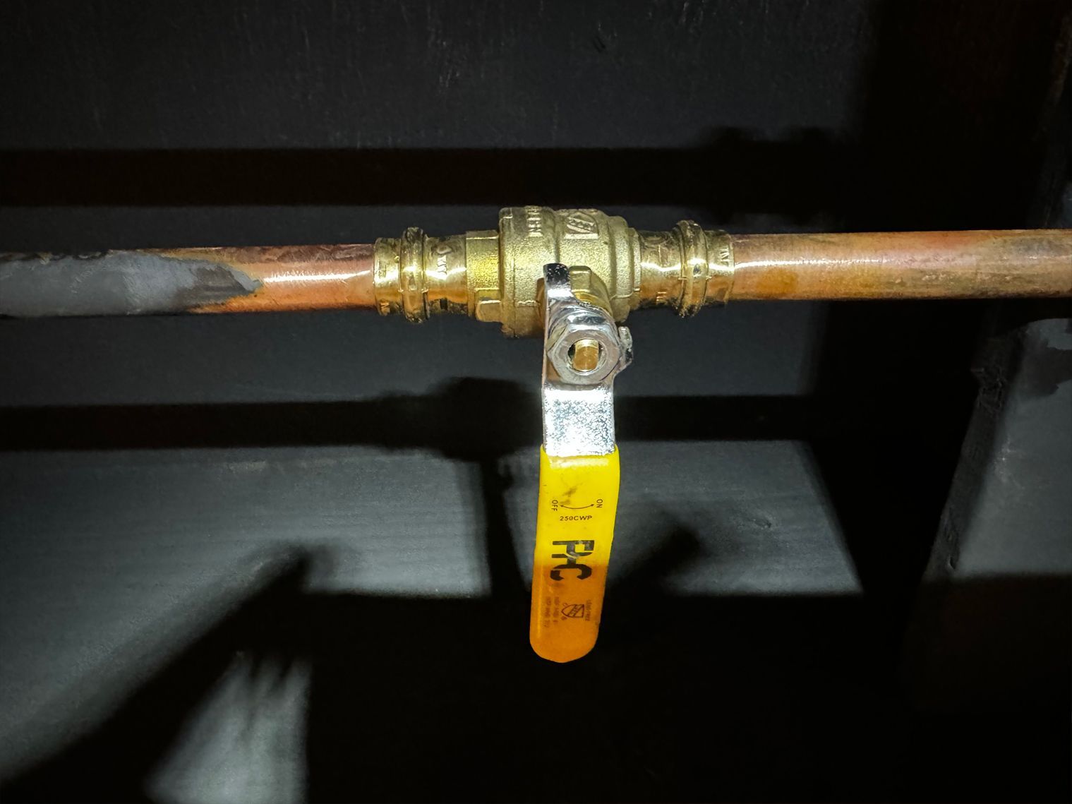 Copper pipe with a brass ball valve and yellow handle, indoors.