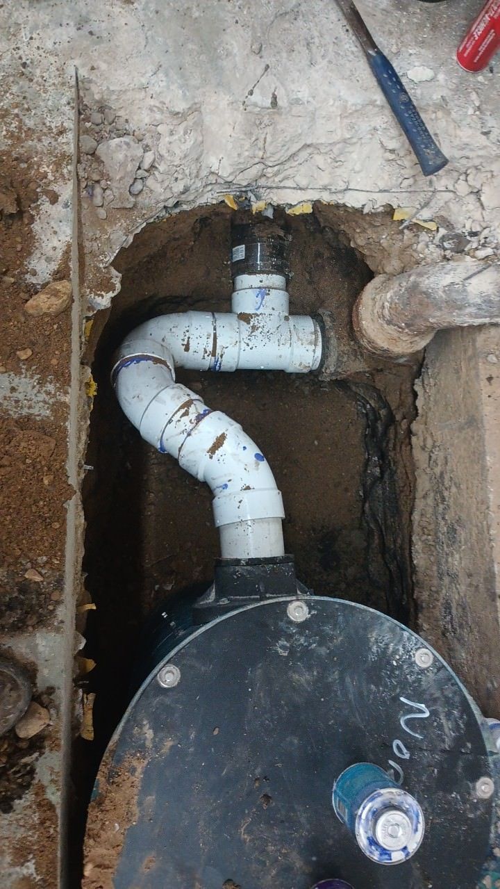 A black cylindrical tank with white PVC pipes in an excavated concrete area.