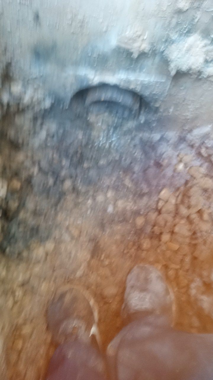 Feet in work boots standing near a dark opening in a dirt pit.