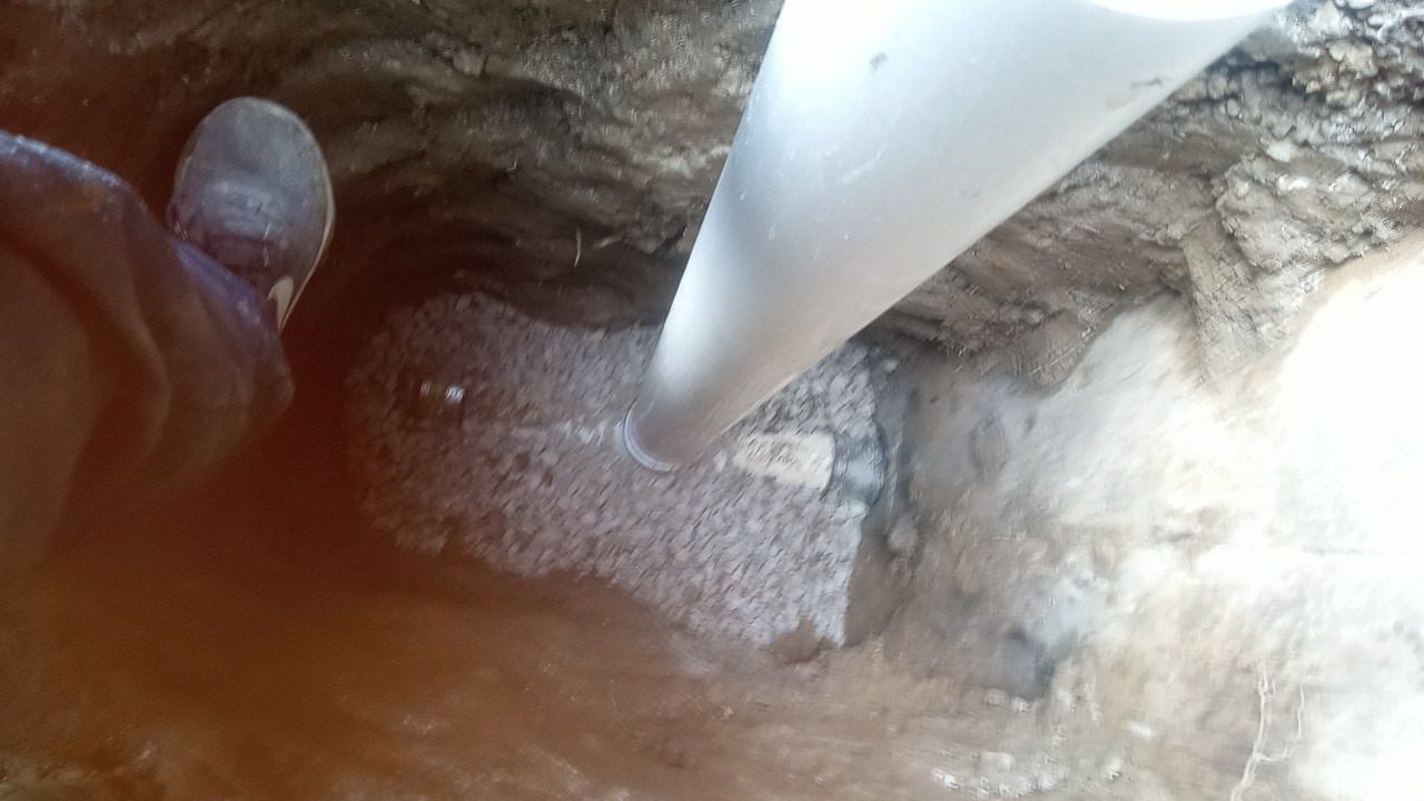 White pipe inserted into a hole in the ground, close up view.