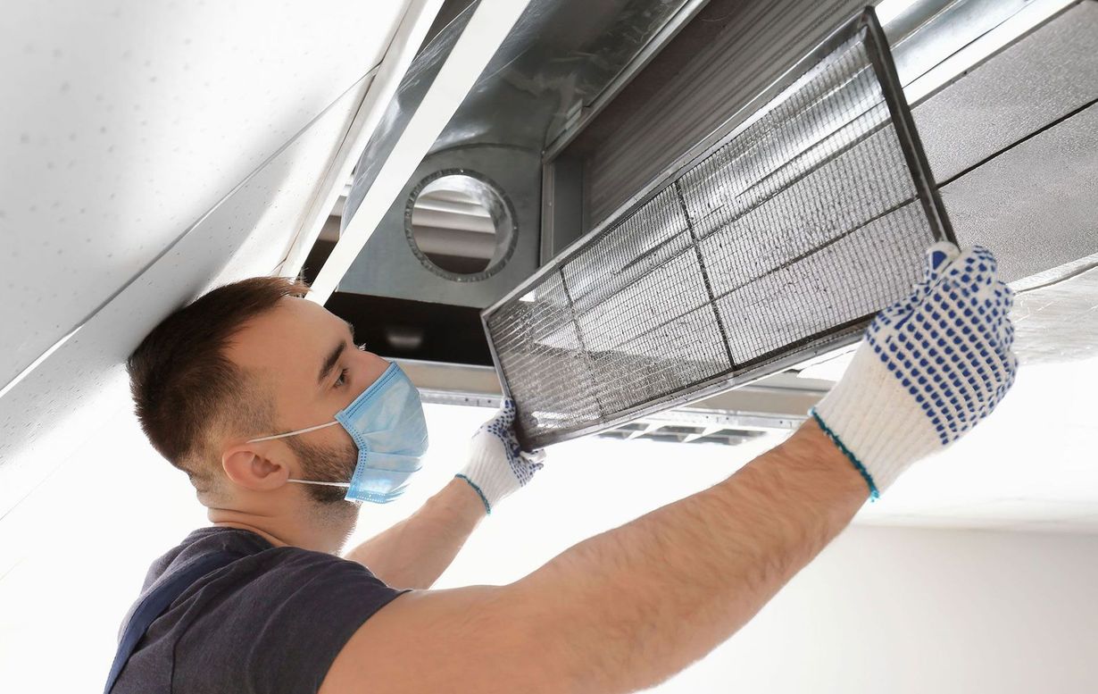Man in mask and gloves replacing air filter in ductwork.