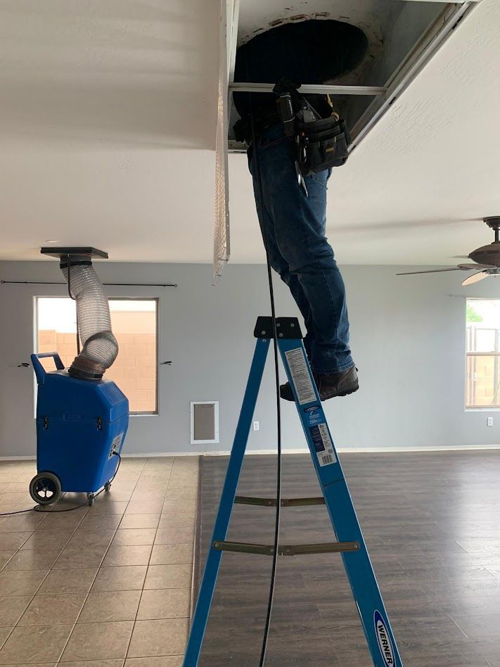 Person on ladder, working on ceiling vent. Blue dehumidifier machine in the room.