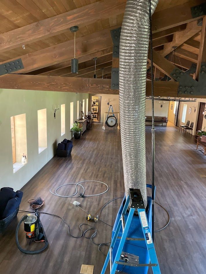 Long open room with wood beams, vinyl flooring, and a large flexible ventilation duct.