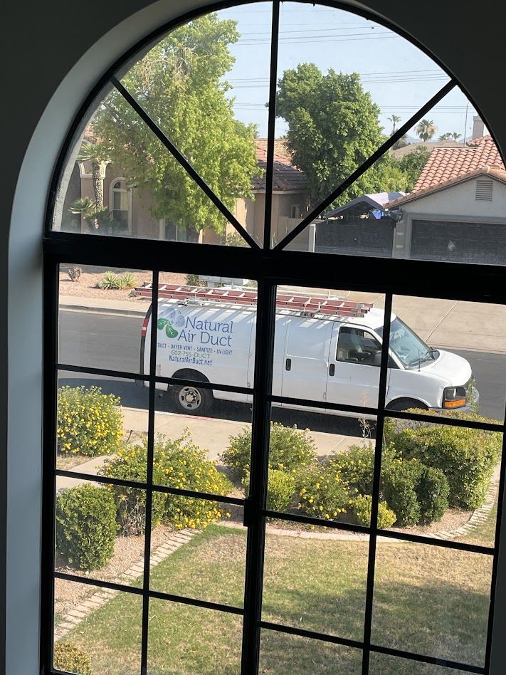 View through a black-framed window of a white van with a ladder parked on a street near a house with a red roof.