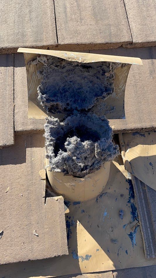 Bird nest debris blocking a roof vent opening.  Gray nest material, tan tiles.