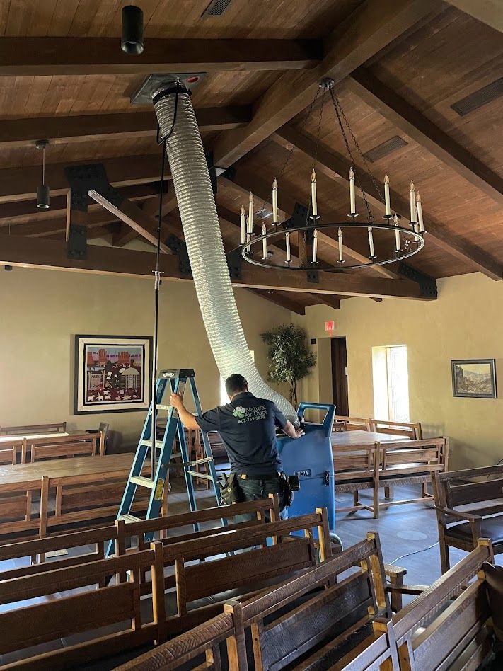 Man using equipment to clean a room with wooden beams and pews.