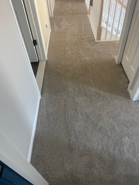 A hallway with a carpeted floor and stairs in a house.