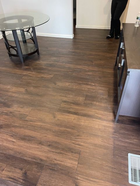 A wooden floor with a glass table and a person standing in the background.
