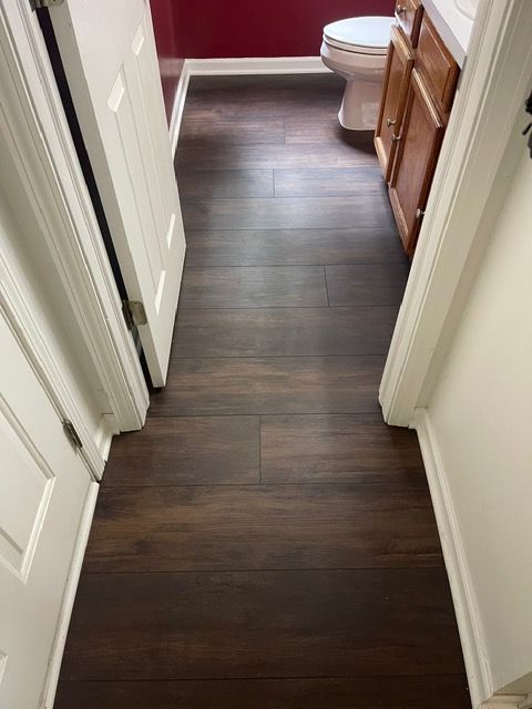 A hallway leading to a bathroom with hardwood floors and a toilet.