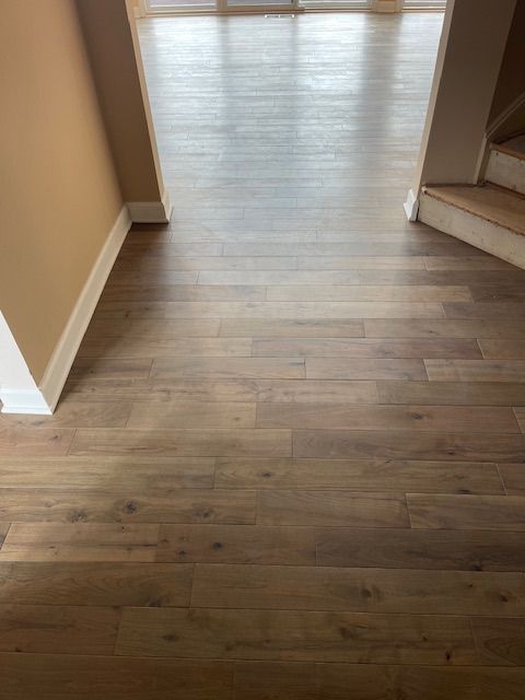 A wooden floor in a hallway with stairs in the background.