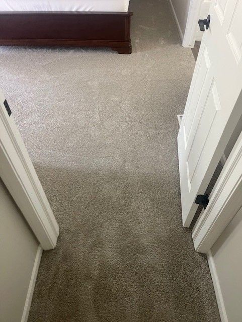 A hallway leading to a bedroom with a bed and a carpeted floor.