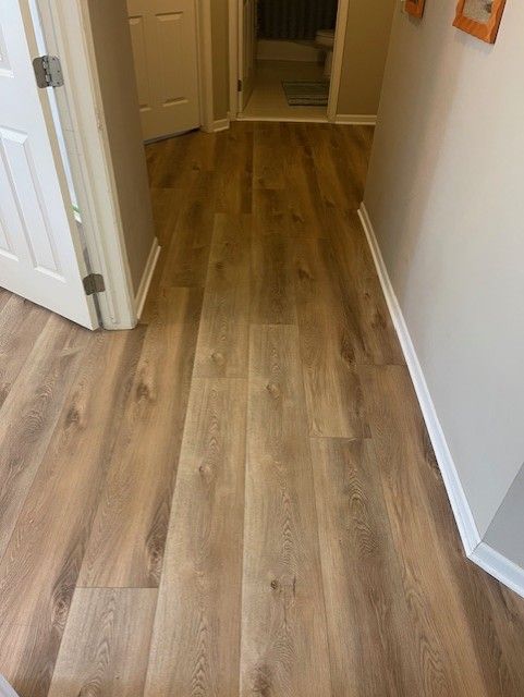 A hallway with hardwood floors and a door leading to a bathroom.