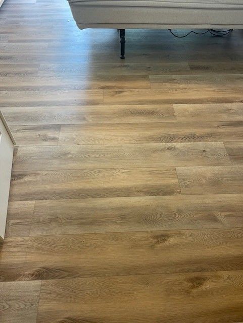 A close up of a wooden floor with a couch in the background.