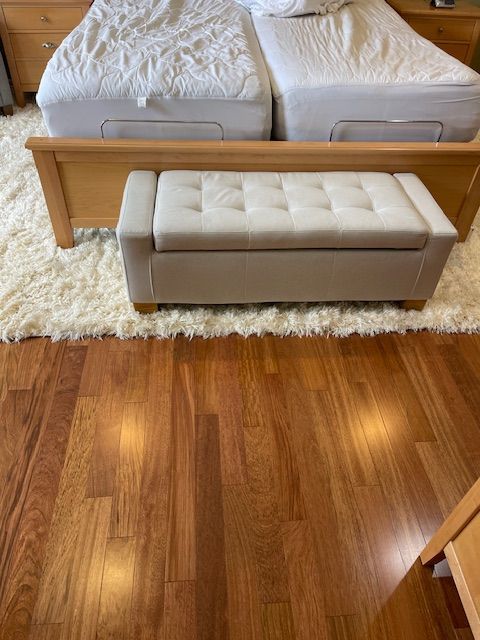A bedroom with two beds and a bench on the floor.